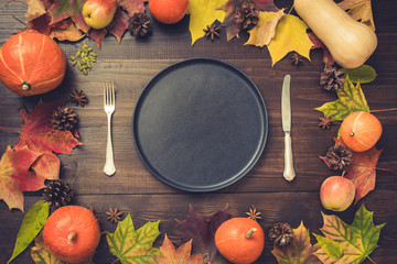 Autumn and Thanksgiving day table setting with fallen leaves, pumpkins, spices, empty black platter and vintage cutlery on brown wooden table. Top view, toned image. © svetlana_cherruty