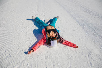 a young woman in a swimsuit and ski pants lying on the snow in winter