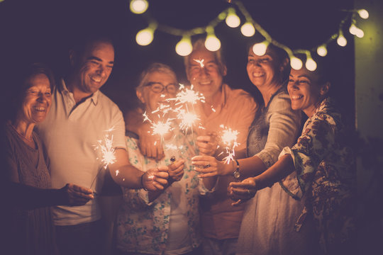 group of caucasian people friends with different ages celebrate together a birthday or new year eve by night outdoor at home. lights and sparkles  with cheerful women and men having fun in friendship