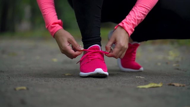 Running shoes - woman tying shoe laces, inserts wireless headphones and running through autumn park at sunset. Slow motion