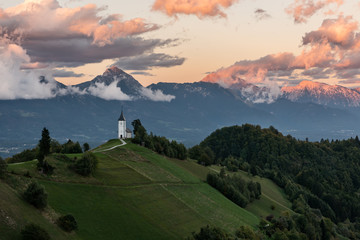 Church on the hill at sunrise. Beautiful scenery at Jamnik, Slovenia. Panoramic view of the Alps behind the church. - obrazy, fototapety, plakaty
