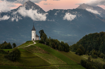 Church on the hill at sunrise. Beautiful scenery at Jamnik, Slovenia. Panoramic view of the Alps behind the church. - obrazy, fototapety, plakaty