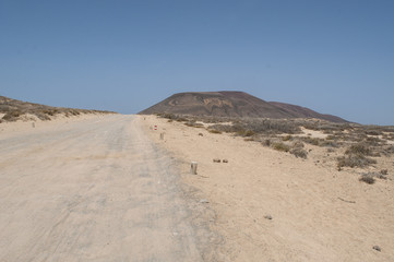 Lanzarote, Isole Canarie: strada sterrata, cespugli e paesaggio desertico con la Montagna Pedro Barba, il vulcano dell'isola La Graciosa