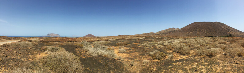 Lanzarote, Isole Canarie: strada sterrata, cespugli e paesaggio desertico con la Montagna Pedro Barba, il vulcano dell'isola La Graciosa