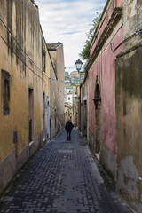 Fototapeta na wymiar un vecchio con bastone cammina lungo una via di un caretteristico ed antico Borgo della Sicilia