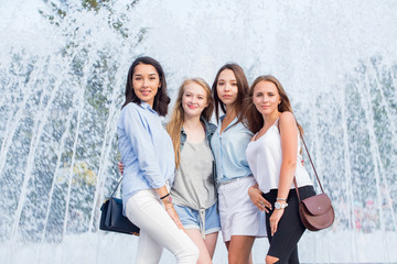 Portrait of beautiful four women near the fountain in the city. Happy girls have fun posing and looking at the camera