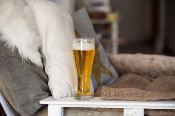 glass of golden beer next to a white, rustic, comfortable chair