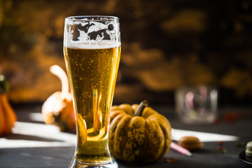 glass of golden beer on dark, wooden table, surrounded by autumn decorations, pumpkins, leaves