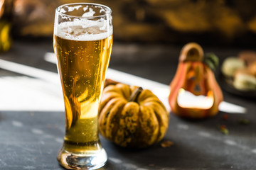 glass of golden beer on dark, wooden table, surrounded by autumn decorations