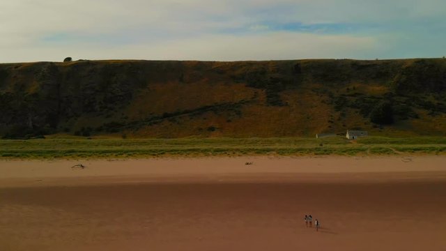 Beautiful views from drone of a long wide beach during low tide under a blue cloudy sky with some views of a family walking along.