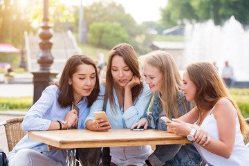 Four attractive young women use smartphones at a table in the Park