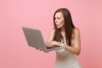 Portrait of shocked bride woman in white wedding dress planning wedding, working on laptop pc computer isolated on pastel pink background. Wedding to do list. Organization of celebration. Copy space.