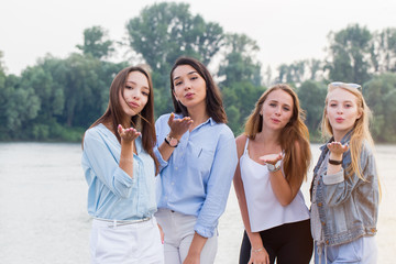 four attractive young women standing and sending kisses at camera outdoor.