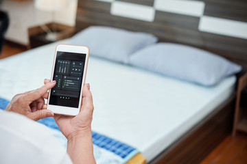 Close-up of unrecognizable mature woman holding smartphone and using music player app on blurred background of bed