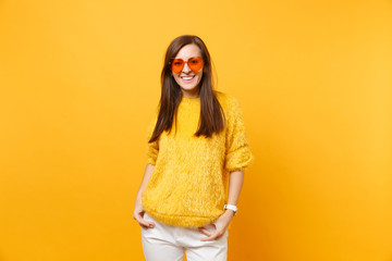 Portrait of smiling young woman in fur sweater, heart orange glasses standing kepping hands in...