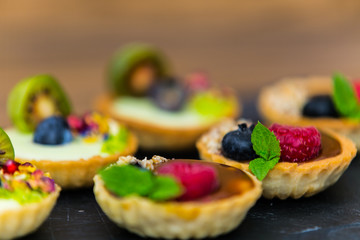 Homemade shortbread tartlets with custard cream and fruit..Tartlets dessert, pastry cakes with fresh fruit on wooden background