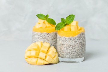Chia seeds pudding with mango puree in beautiful glasses with green mint leaves and cut fresh ripe tropical fruit.