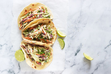 Tacos with guacamole and coleslaw served with lime slices on a light background.