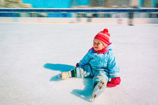 cute little girl sitting on ice with skates, learning skating