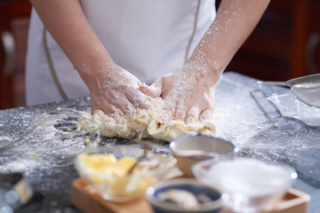 Obraz na płótnie Canvas Close-up view of anonymous woman kneading cookie dough on kitchen table covered with flour
