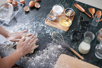 High angle view of unrecognizable woman kneading dough on messy kitchen table with baking...