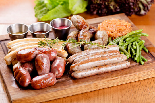 Oktoberfest food menu. Assorted grilled sausages, sauerkraut, green beans on wooden cutting board. Close up