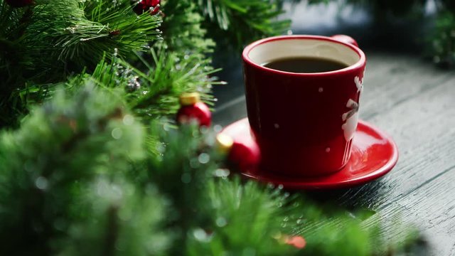 Closeup shot of small cup of fresh hot drink standing on lumber tabletop near fresh conifer branches decorated with small red beads