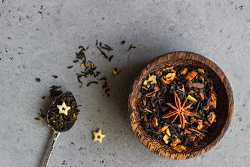 Black dried tea in a wooden bowl, anise and white chocolate stars on grey concrete background. Copy space.