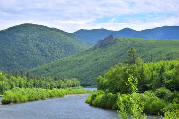 Endless green mountains and river. The mountain the river flows between green hills. At the top of the hill you can see a rock. Lots of green forest and blue sky. The Sikhote-Alin.