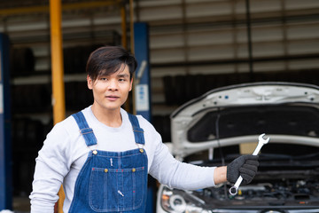 Reliable auto mechanic showing wrench  in a modern automobile repair shop