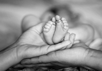 Closeup of parents hands holding newborn baby feet with wedding rings. The concept of the family....