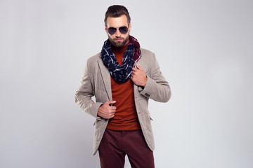 Perfect autumn look. Handsome young man in scarf and glasses looking at camera while standing against white background