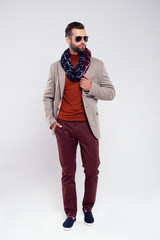 Perfect look for this city. Full length of handsome young man in scarf and glasses looking away while standing against white background