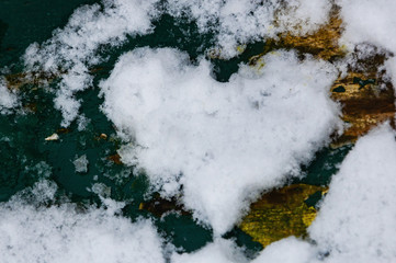 Heart carved in snow covered bench. Selected focus on melting snow on left side. Fragile love ending relations concept.