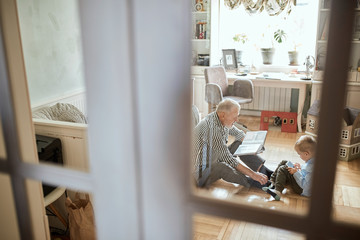 Mature man looking photo book and his grandson using digital tablet
