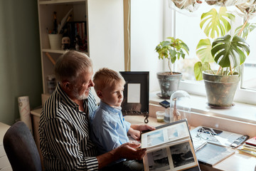 Grandfather and grandson sitting at couch and watch family album