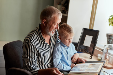 Grandfather and grandson sitting at couch and watch family album