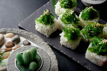 Green sushi set with chuka served on black clay plate with soy sauce and chopsticks, top view. Delicious traditional Japanese food, sushi restaurant concept