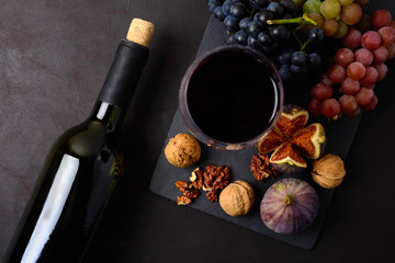 Wineglass with red wine, bottle, grapes, figs and walnuts lying on dark wooden background. Top view. Flat lay. Copy space