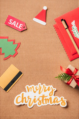 top view of credit card, sale sign, decorated gift box and merry christmas lettering on surface