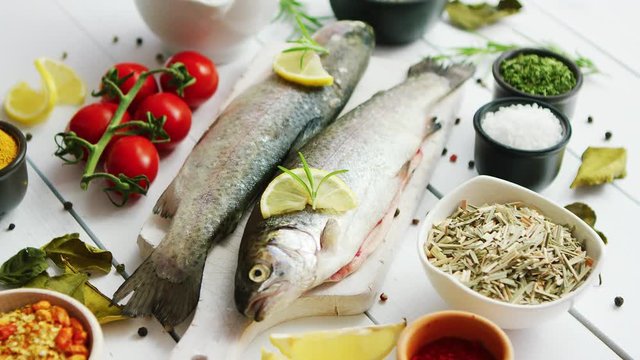 Various aromatic spices and bunch of fresh tomatoes lying on white wooden tabletop around cutting board with fresh trout