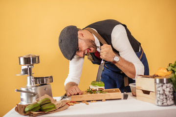 The funny man in cap and classy wear is ready to perform a show to demonstrate how delicious this hamburger is. He is about to make a big bite from green burger.