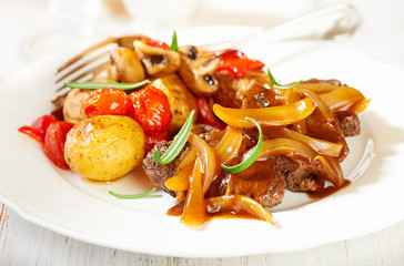 Braised beef with onion sauce and oven baked vegetables. Homemade food. Concept for a tasty and hearty dish. White wooden background. 