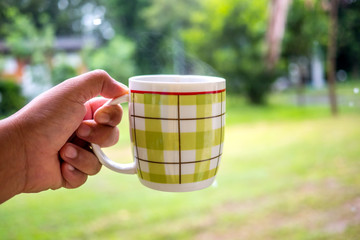 Modern coffee cup in hand on Green blur background.Tea cup on nature.