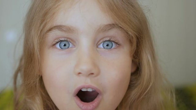 Girl looks and is surprised and happy to receive a surprise. Portrait little young girl with blue eyes looking at camera. Closeup