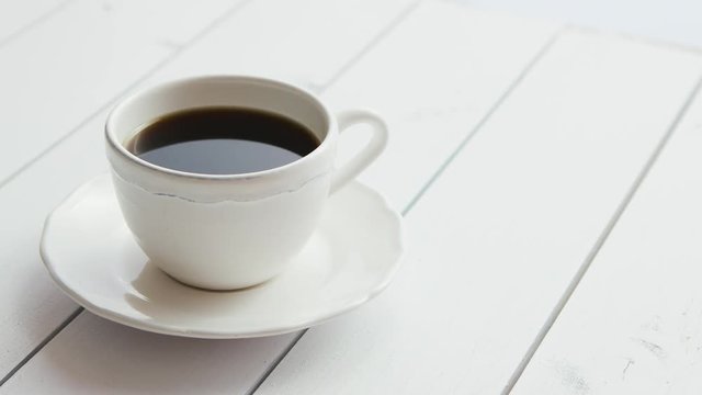 From above view of white cup of hot black coffee with saucer laid on wooden background