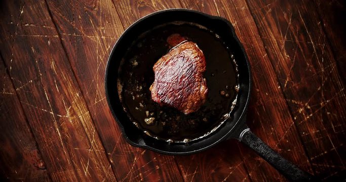 From above view of fresh fried meat in cooking oil placed on black pan on wooden background