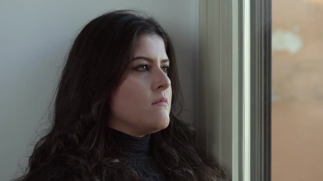 Pensive sad young woman at the window. Worries, thoughts, sadness