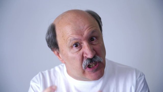 Disappointed and angry man point his finger in facial emotion expression of senior 60s 70s year old man in studio on grey background in face expression concept. 