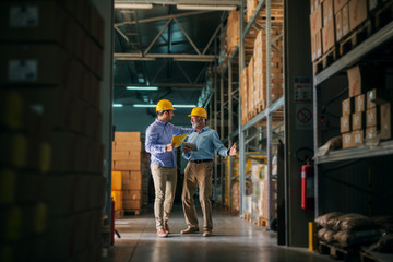 Picture of two business man standing in warehouse with helmets on their heads and celebrating great...